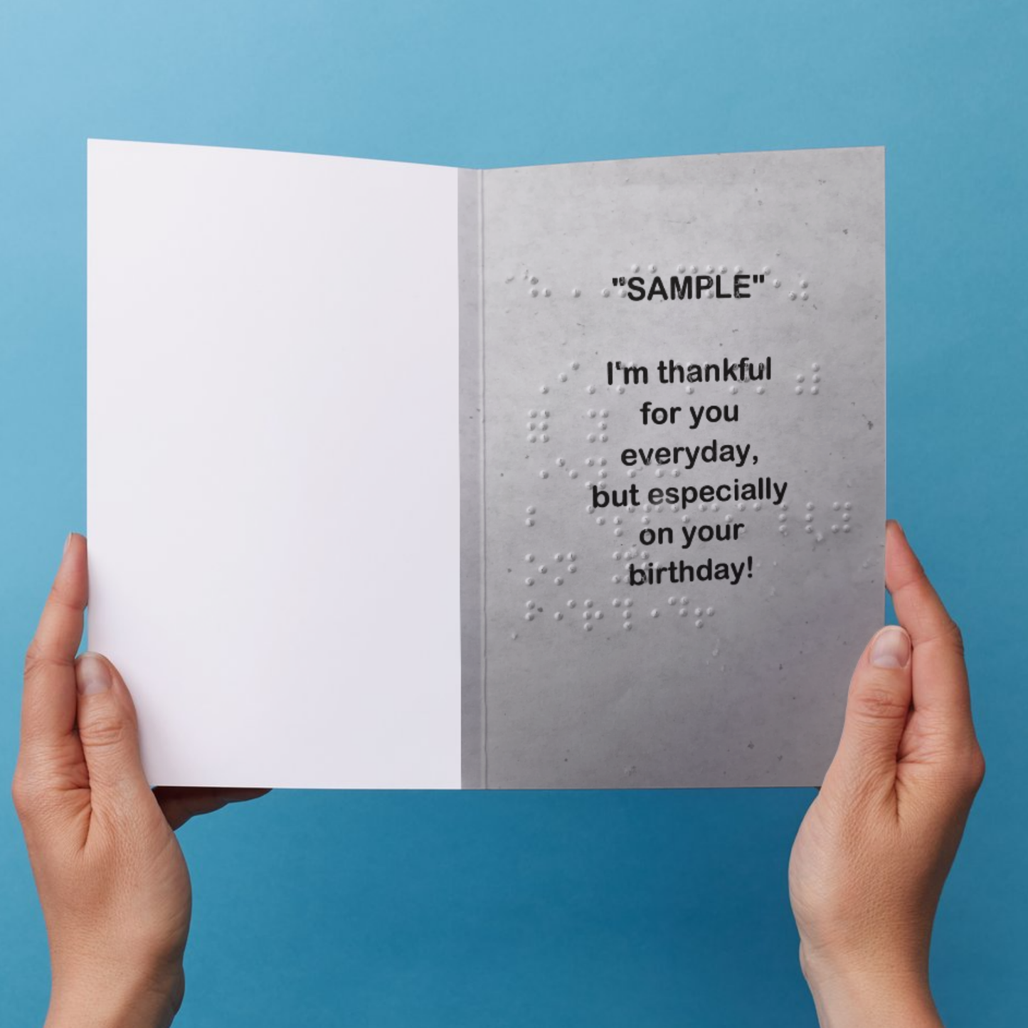 Card with braille text held by hands against a blue background