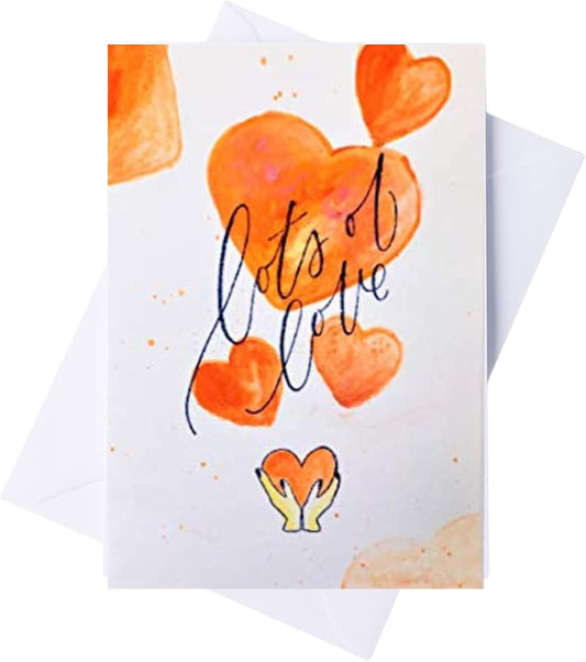 A greeting card with a white background, featuring orange watercolor hearts, the phrase 'lots of love' in black script, and a small yellow-and-orange heart hands illustration. A white envelope is partially visible behind the card.