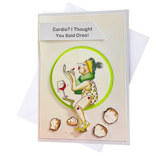 A novelty greeting card with a white envelope behind it. The card features a cartoon illustration of a woman applying lipstick while looking at a mirror, with a glass of red wine and several Oreo cookies.