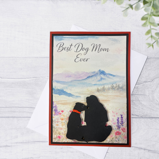 Greeting card with silhouette of a woman and dog sitting together, text 'Best Dog Mom Ever', on a scenic background.