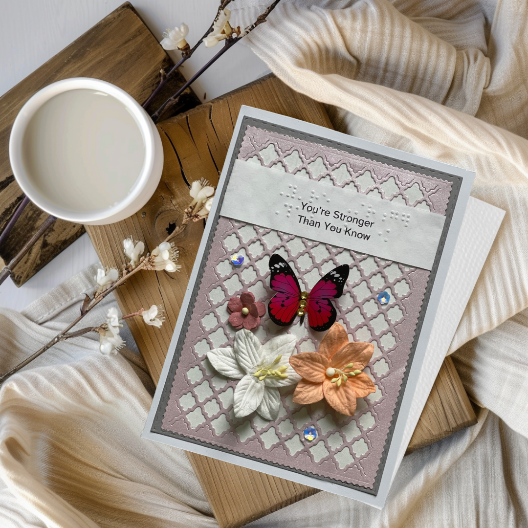 Greeting card with butterfly and flowers on a wooden surface with a cup and branches.