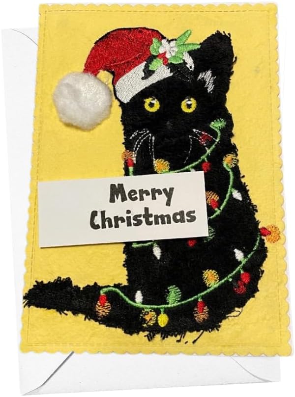 A handmade Christmas card featuring an embroidered black cat wearing a red Santa hat and wrapped in a green Christmas light garland, with a white paper label reading 'Merry Christmas' across the front, shown with a white envelope.