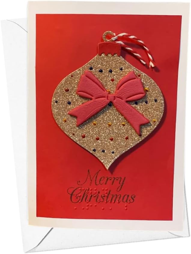A Christmas greeting card with a red background and a large glittery gold ornament design in the center, accented by a red ribbon bow and a red-and-white striped hanging loop. The card reads 'Merry Christmas' in black script near the bottom, and a white envelope is partially visible behind it.