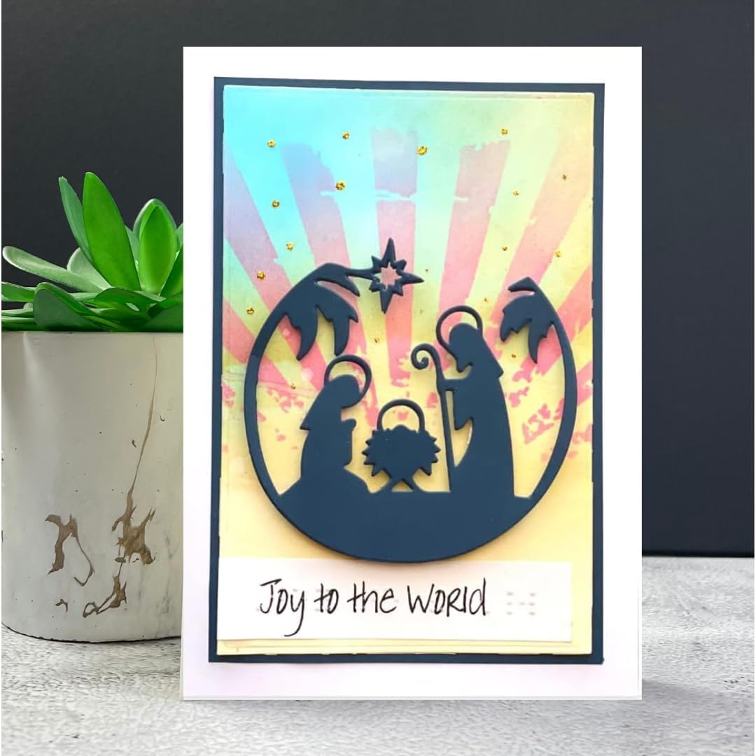 A handmade greeting card featuring a navy blue silhouette of the Holy Family (Mary, Joseph, and baby Jesus) under a star, set against a pastel sunburst background with gold glitter accents. The card has a white border and the text 'Joy to the World' written on a white strip at the bottom.