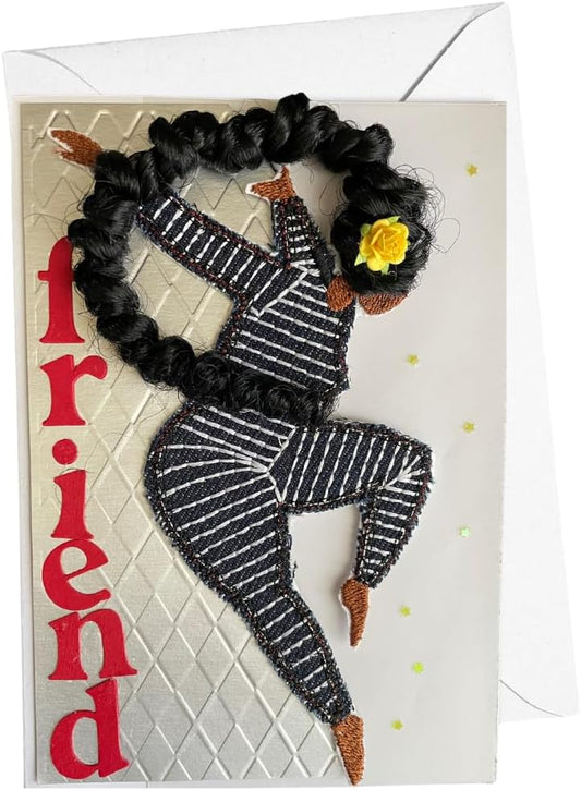 A greeting card featuring a stylized stitched figure of a dancing person with black braided hair, a yellow flower accent, and the word 'friend' in red vertically along the left side. The card is shown with a white envelope behind it on a white background.