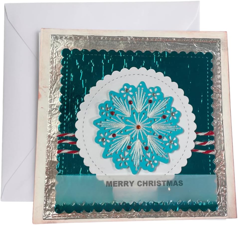 A square Christmas greeting card with a white envelope behind it. The card features a metallic silver border, a deep teal background, a large white scalloped circle, and a bright turquoise snowflake design in the center with small red and silver accents.