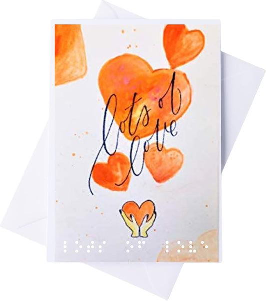 A square greeting card with a white background, featuring orange watercolor hearts, the phrase 'let's all love' in black script, a small yellow heart at the bottom, and white Braille text. A white envelope is partially visible behind the card.