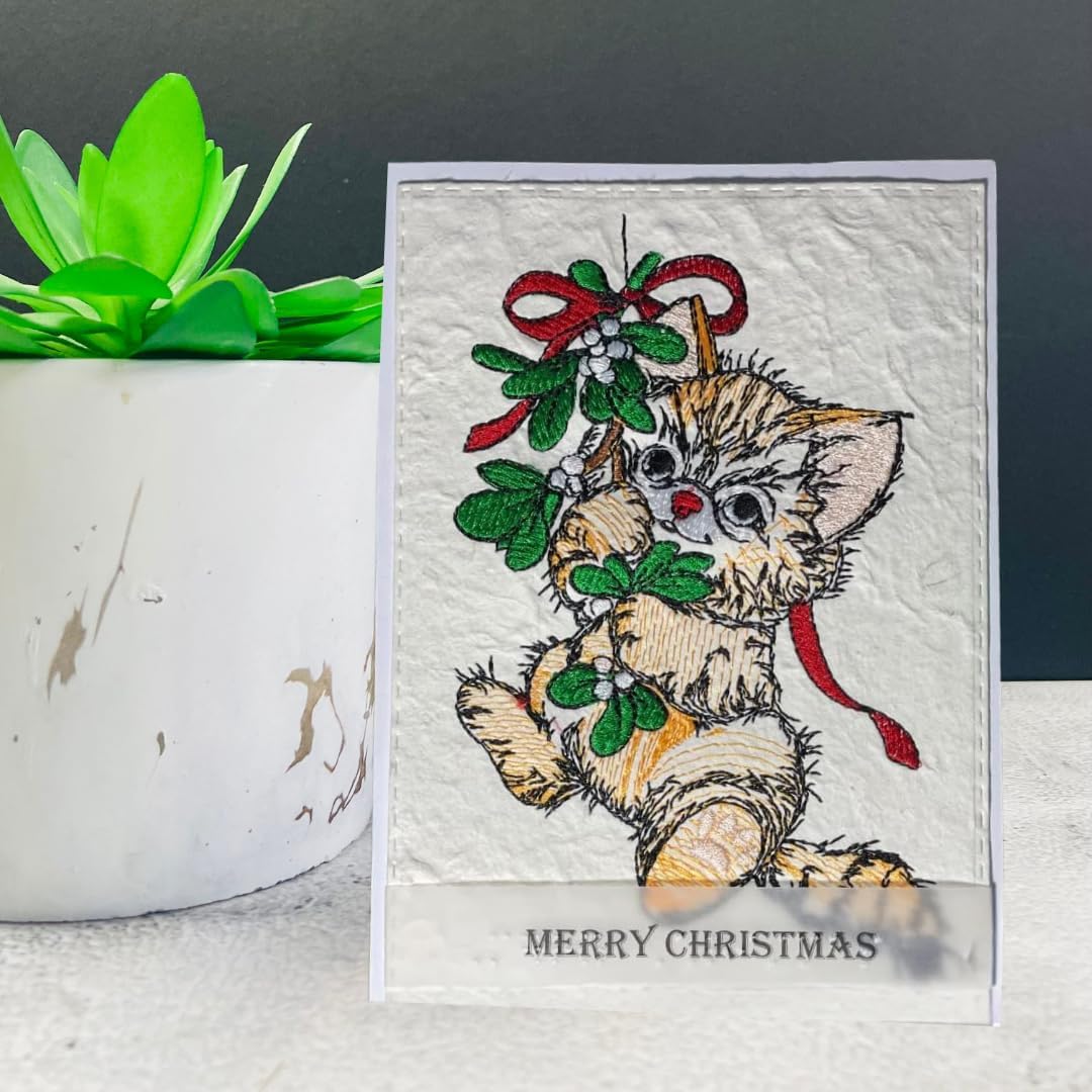 A handmade Christmas greeting card featuring a detailed embroidery of a kitten eating mistletoe, displayed on a white surface next to a green succulent in a white pot.