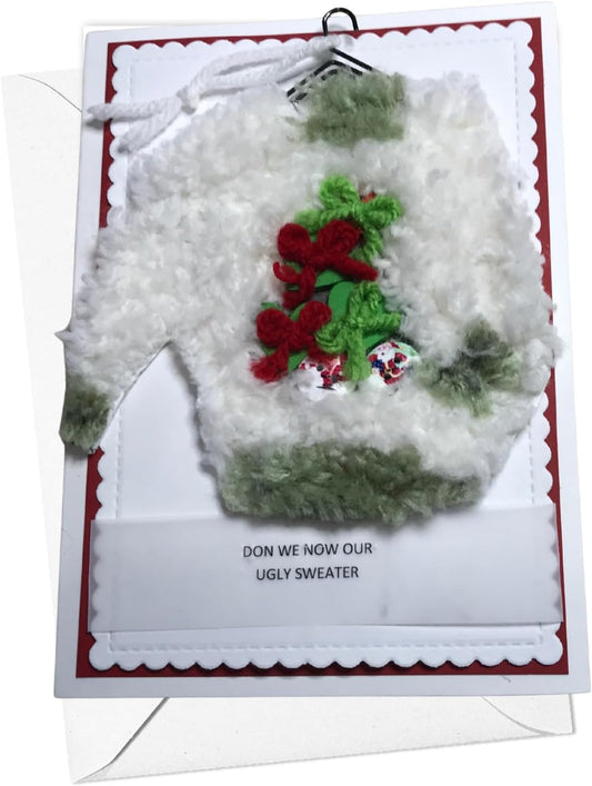 A novelty greeting card featuring a fluffy white sweater with green trim and a red embroidered holly design. The card has a printed message at the bottom that reads 'DON WE NOW OUR UGLY SWEATER' and is photographed against a white background.