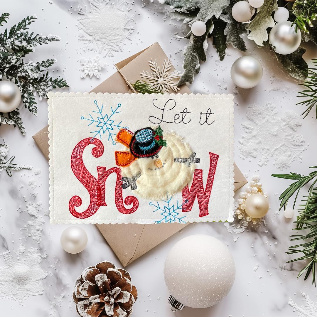 A festive handmade greeting card with the words 'Let it Snow' in red and white, decorated with a small snowman figure, surrounded by a kraft envelope and styled with Christmas greenery, ornaments, and snow on a white marble surface.