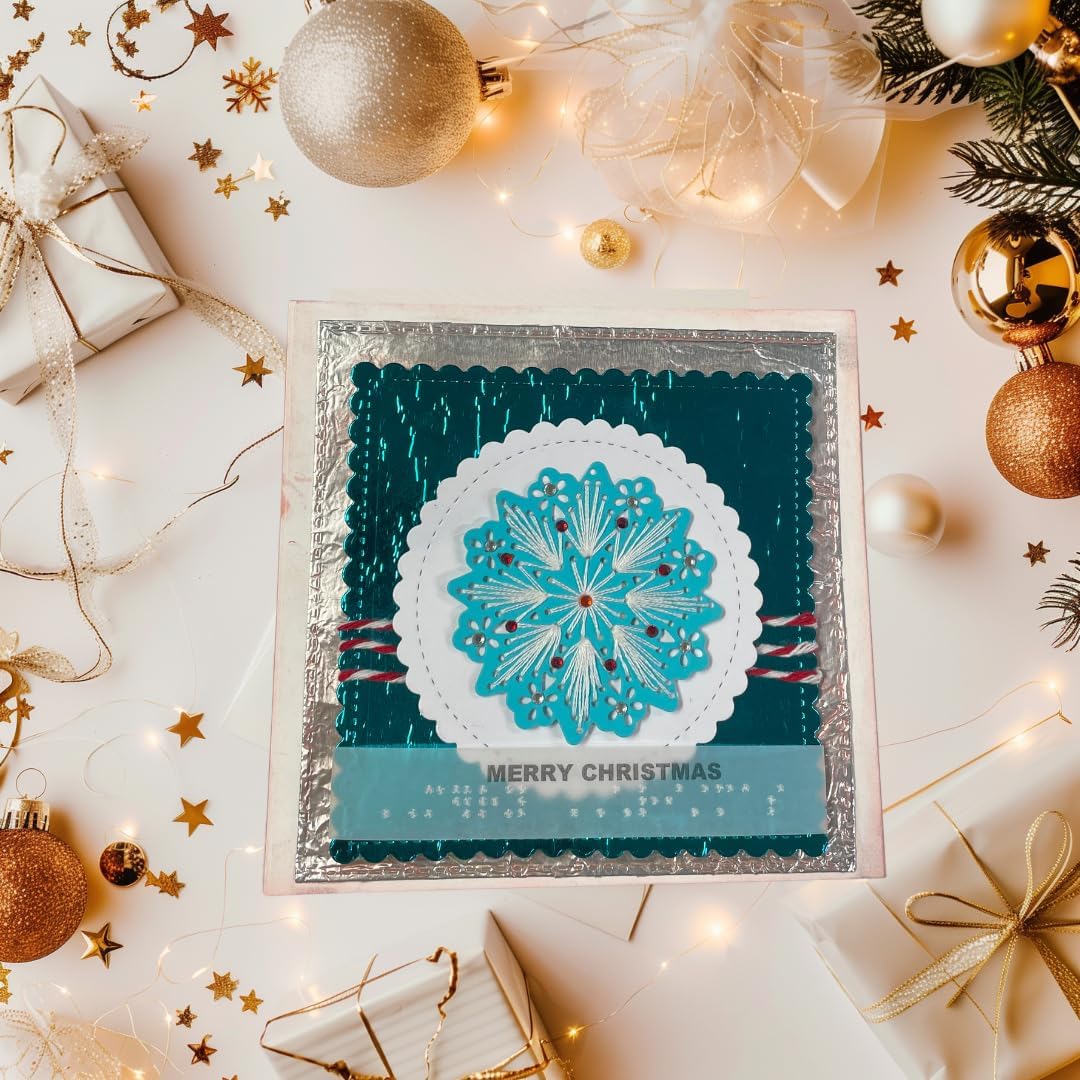 A square handmade Christmas card with a teal and turquoise snowflake design, displayed on a decorated flat-lay surface with gold ornaments, gift boxes, and fairy lights.