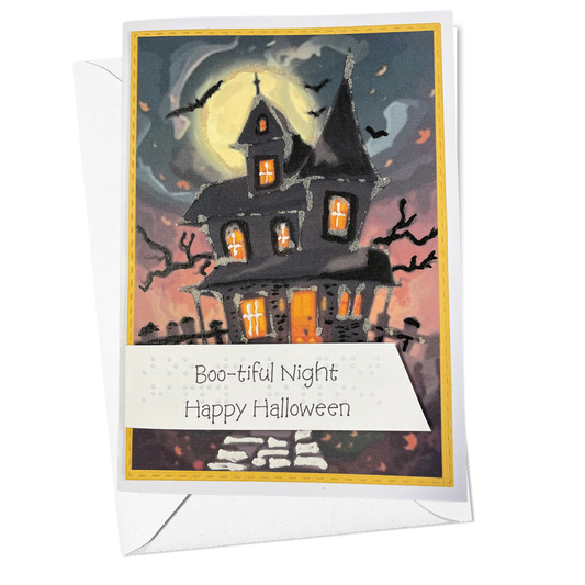 A Halloween greeting card with a white envelope, featuring an illustration of a spooky haunted house under a full moon with the text 'Boo-tiful Night Happy Halloween'.