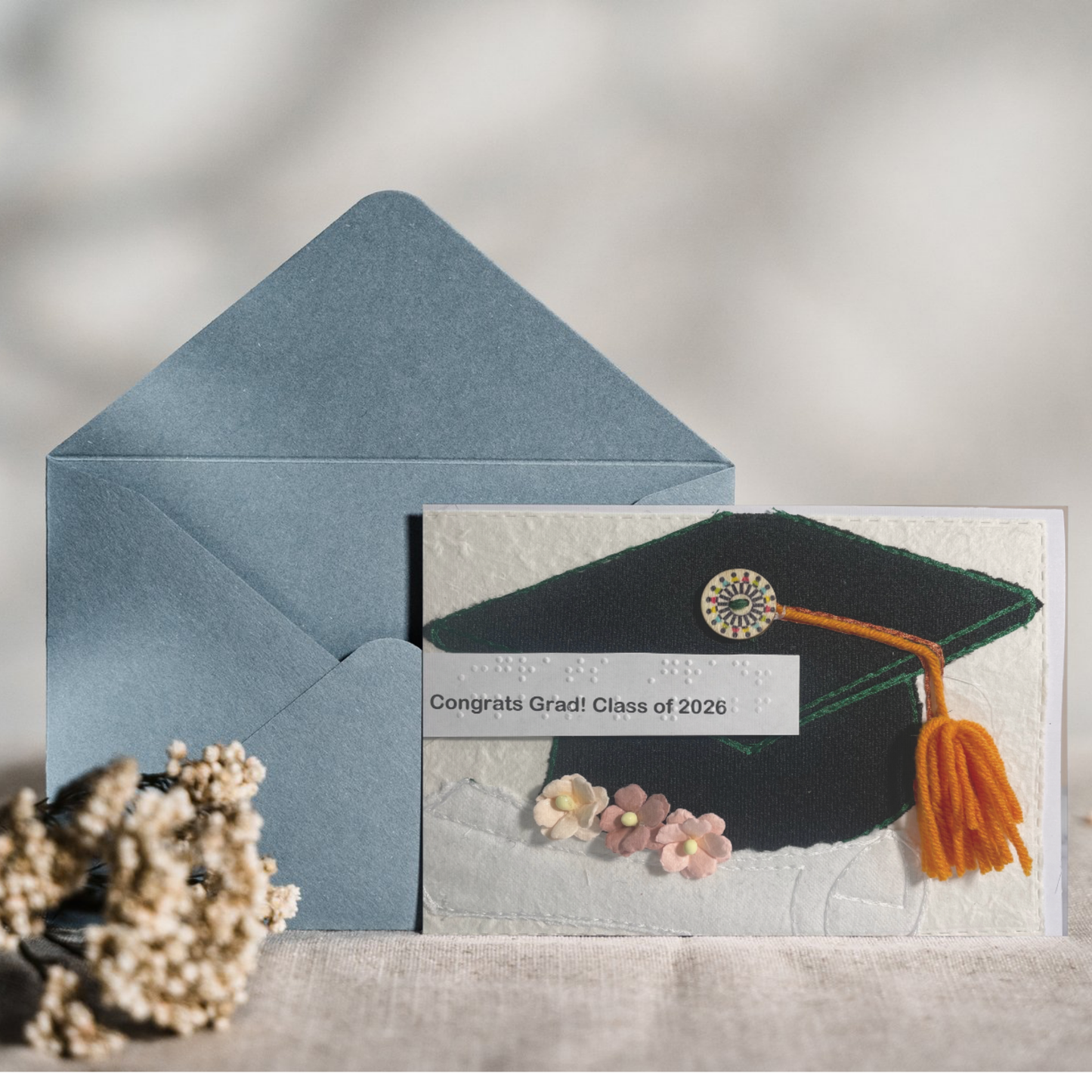 Graduation-themed card with mortarboard and tassel, accompanied by a blue envelope on a textured surface.