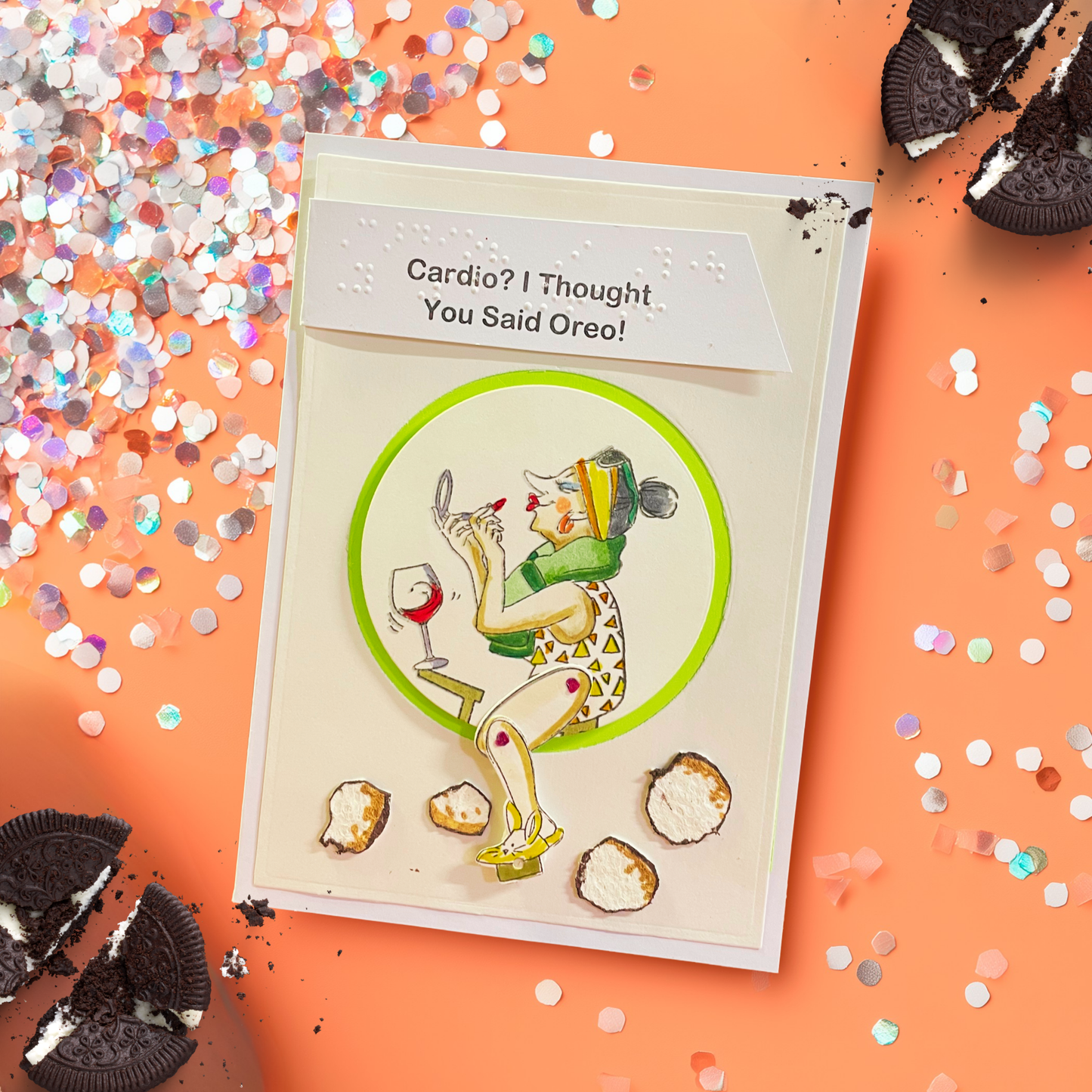 A handmade greeting card featuring a whimsical illustration of a woman exercising while holding a wine glass, with the text 'Cardio? I Thought You Said Oreo!'. The card is styled on an orange background with scattered Oreo cookies, silver glitter, and confetti.