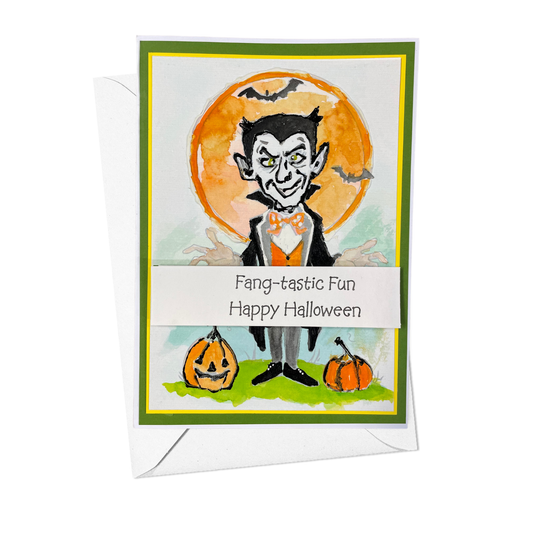 A Halloween greeting card with a white envelope behind it, featuring a cartoon vampire in front of an orange full moon, with jack-o'-lanterns at the bottom and the text 'Fang-tastic Fun Happy Halloween'.