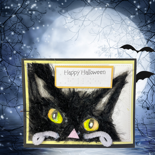 A handmade Halloween greeting card featuring a black cat made from black yarn and white pipe cleaners, with a 'Happy Halloween' label, set against a spooky full moon and bats background.