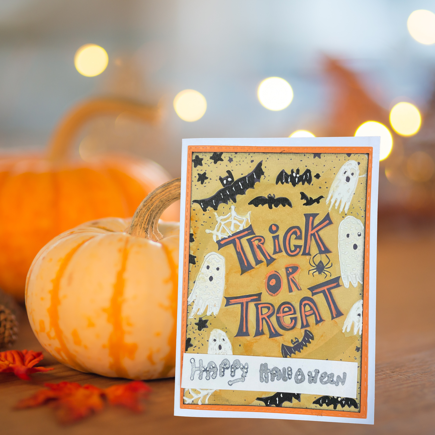 A Halloween greeting card with 'Trick or Treat' and 'Happy Halloween' text, styled on a wooden surface with pumpkins and warm string lights in the background.