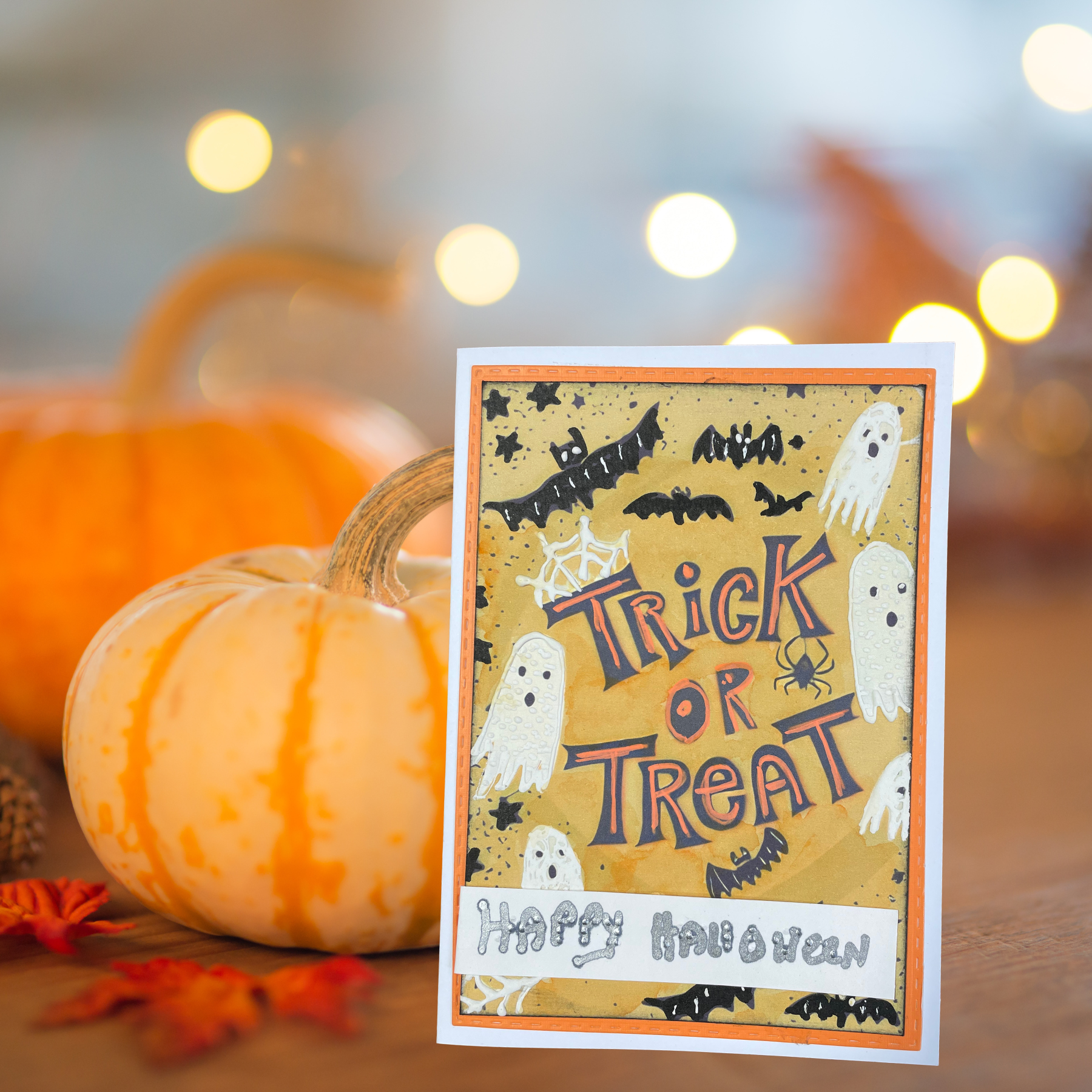 A Halloween greeting card with 'Trick or Treat' and 'Happy Halloween' text, styled on a wooden surface with pumpkins and warm string lights in the background.