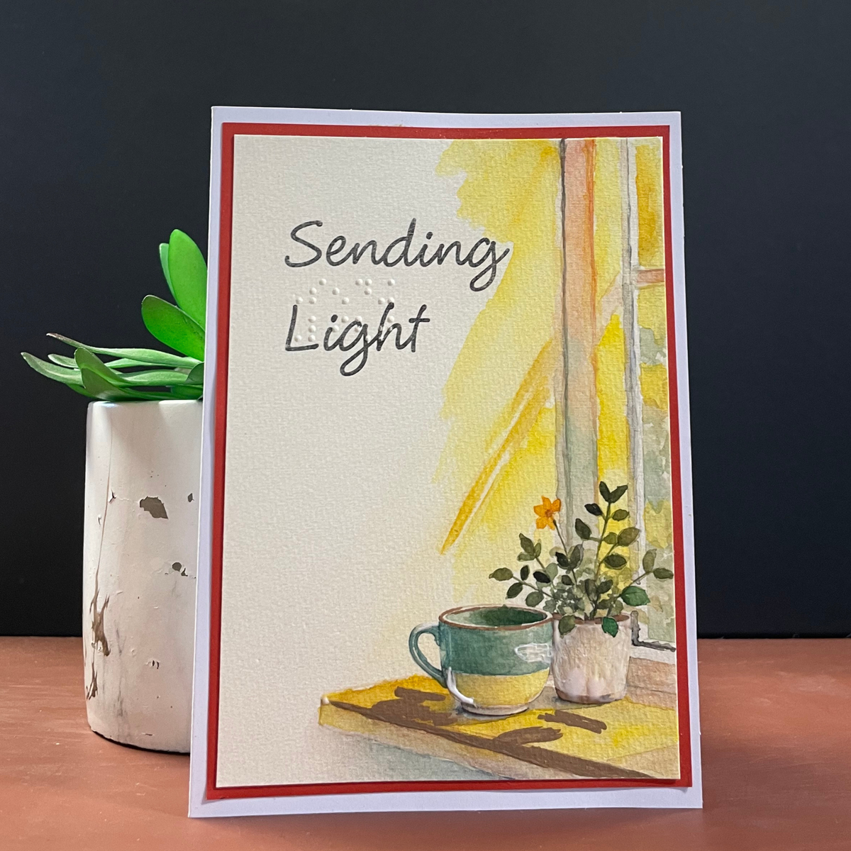 Card front in various display angles — watercolor window scene, teal mug, potted plant, red mat border