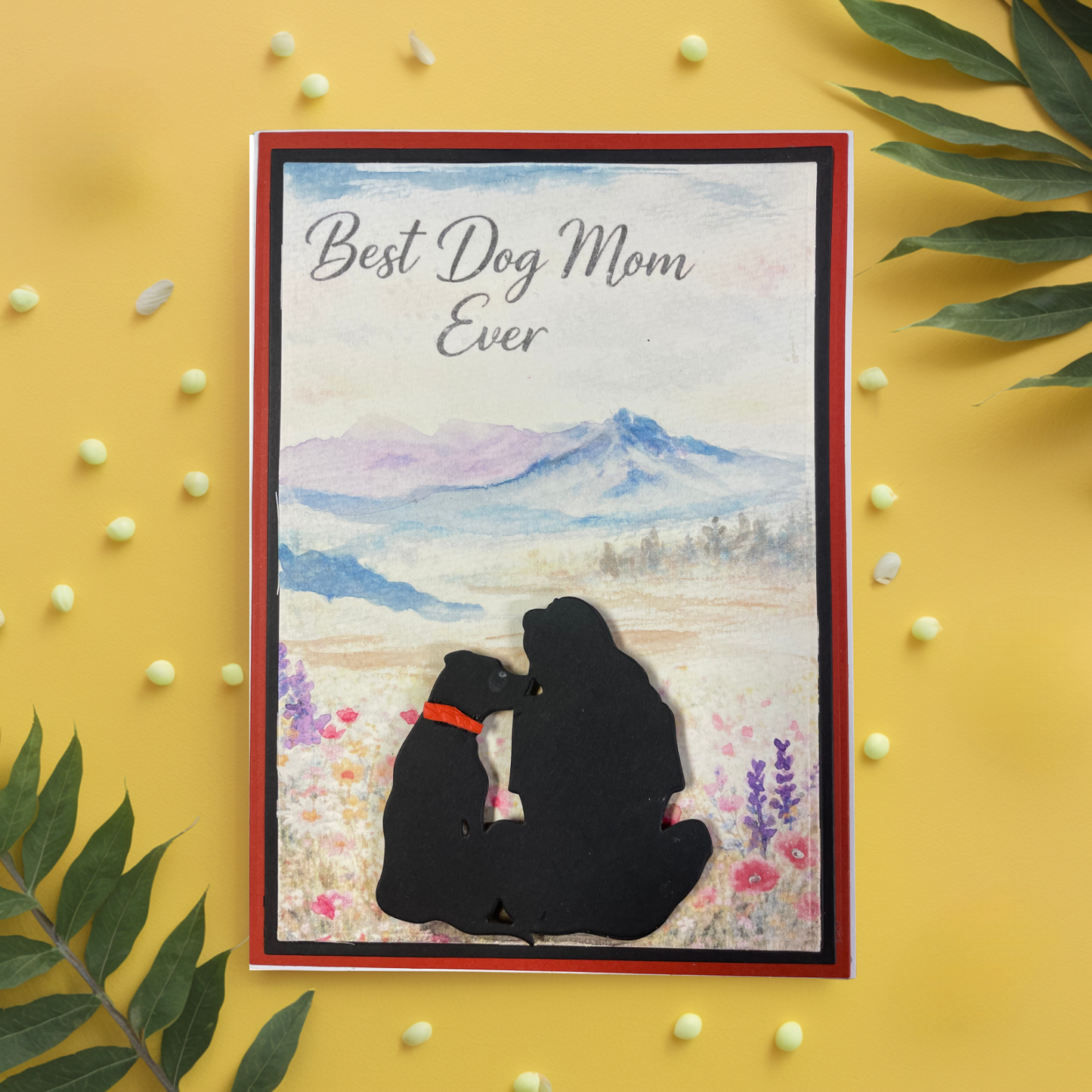 Greeting card with silhouette of a person and her dog and 'Best Dog Mom Ever' text on a scenic background, surrounded by decorative elements.