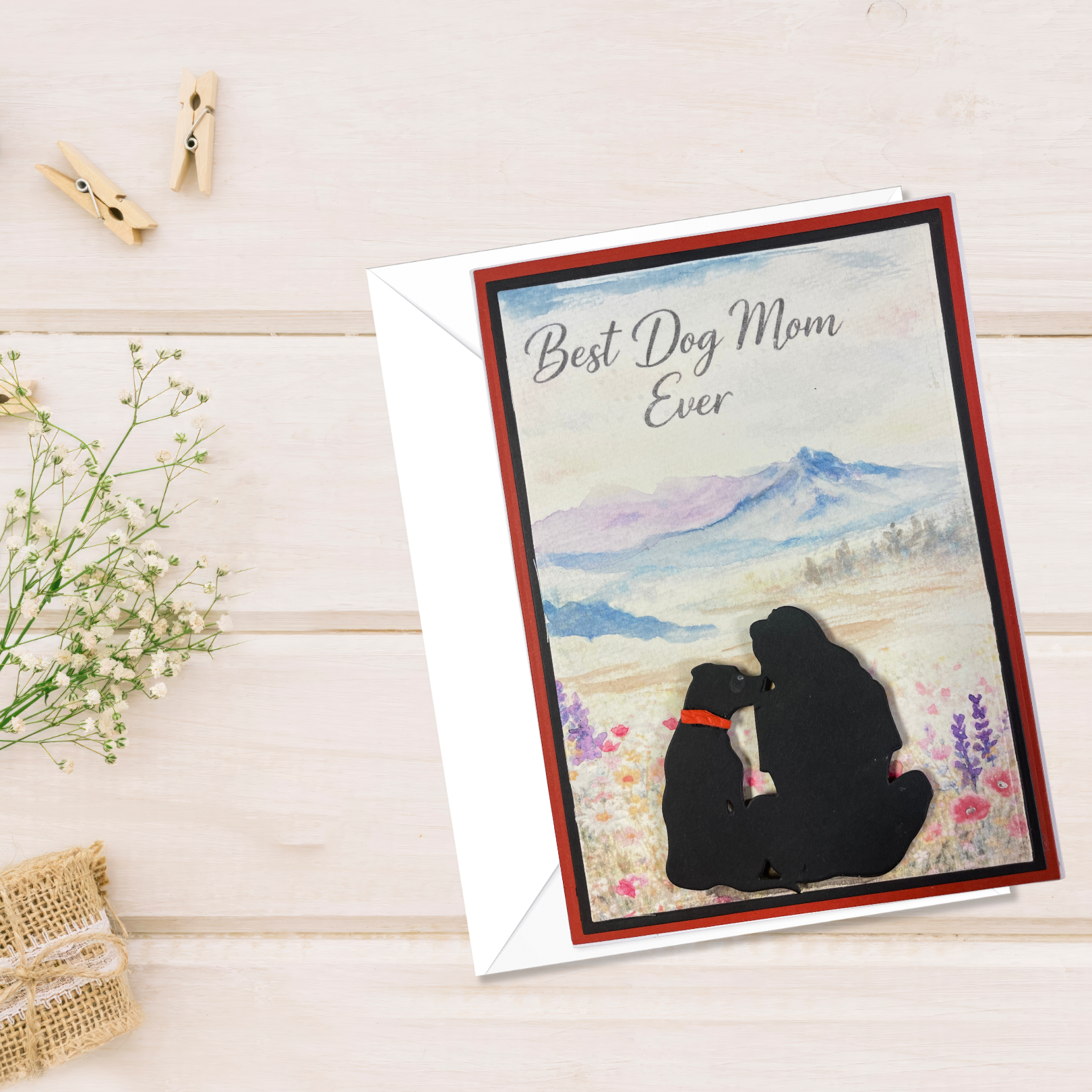 Greeting card with silhouette of a person and dog, text 'Best Dog Mom Ever', on a wooden surface with flowers and clips.