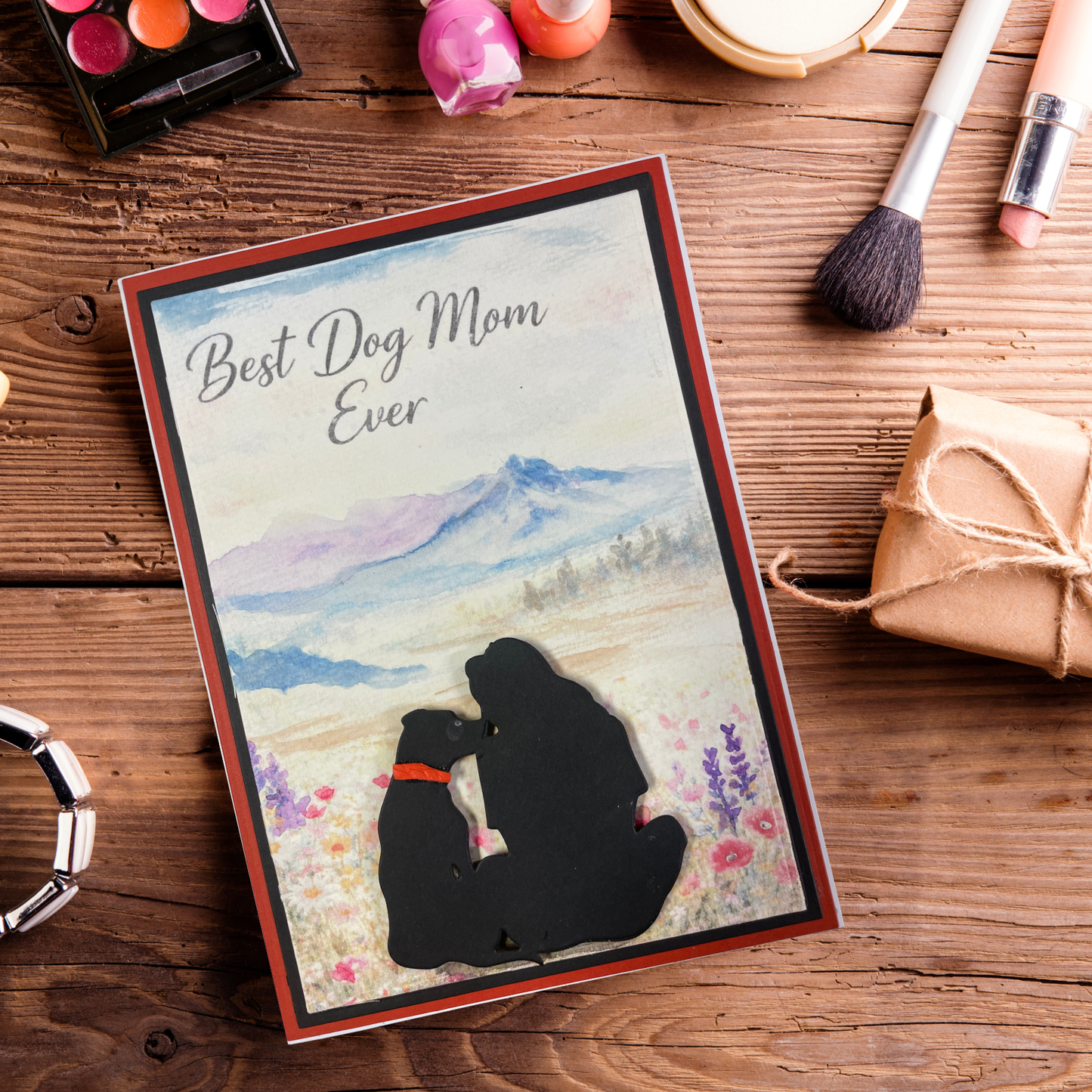Card with 'Best Dog Mom Ever' text and silhouette of a dog and owner on a wooden surface with makeup items.