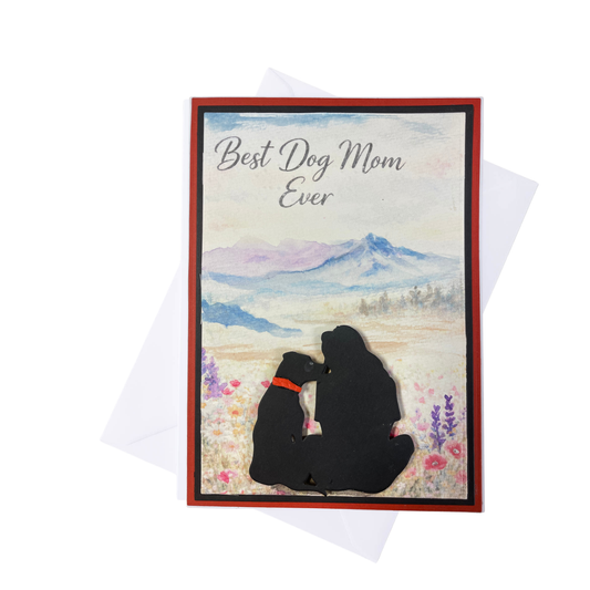   A beautiful black silhouette of a woman and her dog sitting side by side in a wildflower meadow, gazing at a soft watercolor mountain landscape