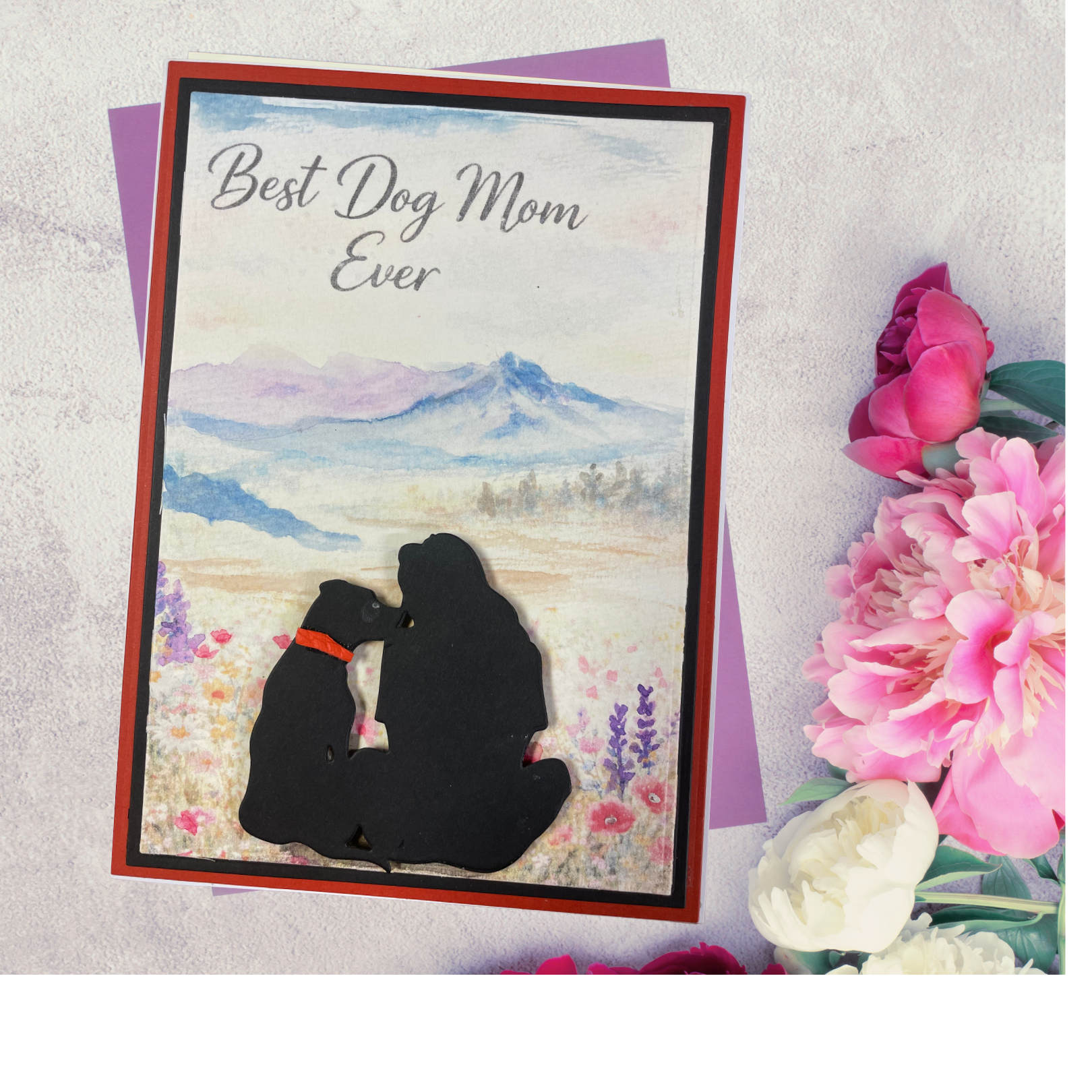  beautiful black silhouette of a woman and her dog sitting side by side in a wildflower meadow, gazing at a soft watercolor mountain landscape — framed by a bold red and black border. 