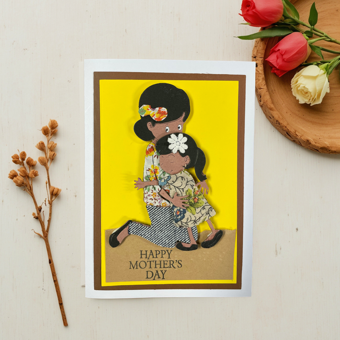 Mother's Day card with tactile image of a woman and child on a yellow background, surrounded by flowers and branches.