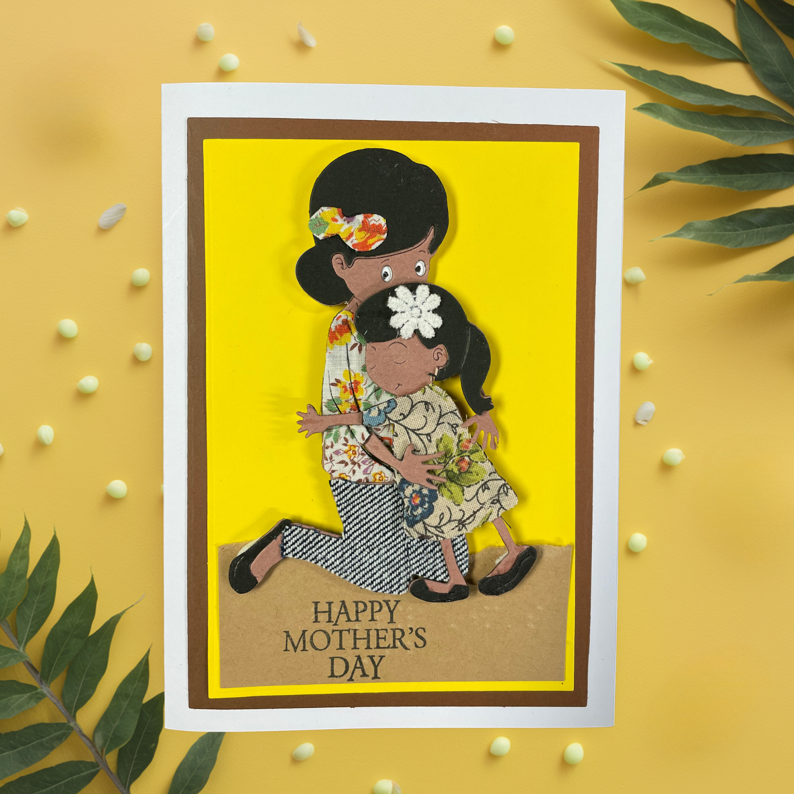 Greeting card with a tactile image of a mother and daughter on a yellow background, featuring 'Happy Mother's Day' text.