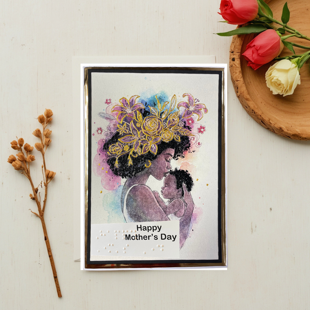 Mother's Day card with a woman holding a child and floral design, placed on a light surface with flowers and branches.