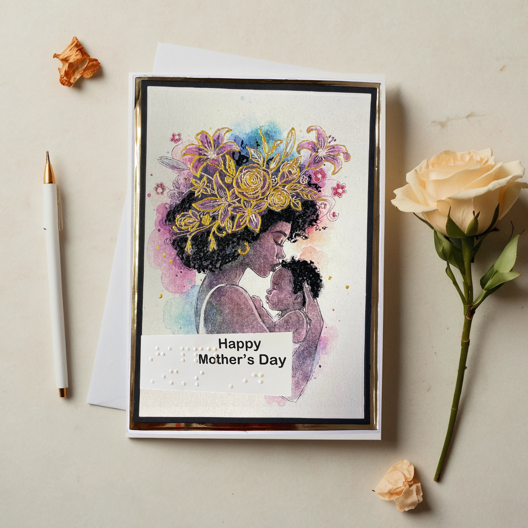 Greeting card with a silhouette of a woman holding a child and 'Happy Mother's Day' text, surrounded by flowers and a pen on a beige background.