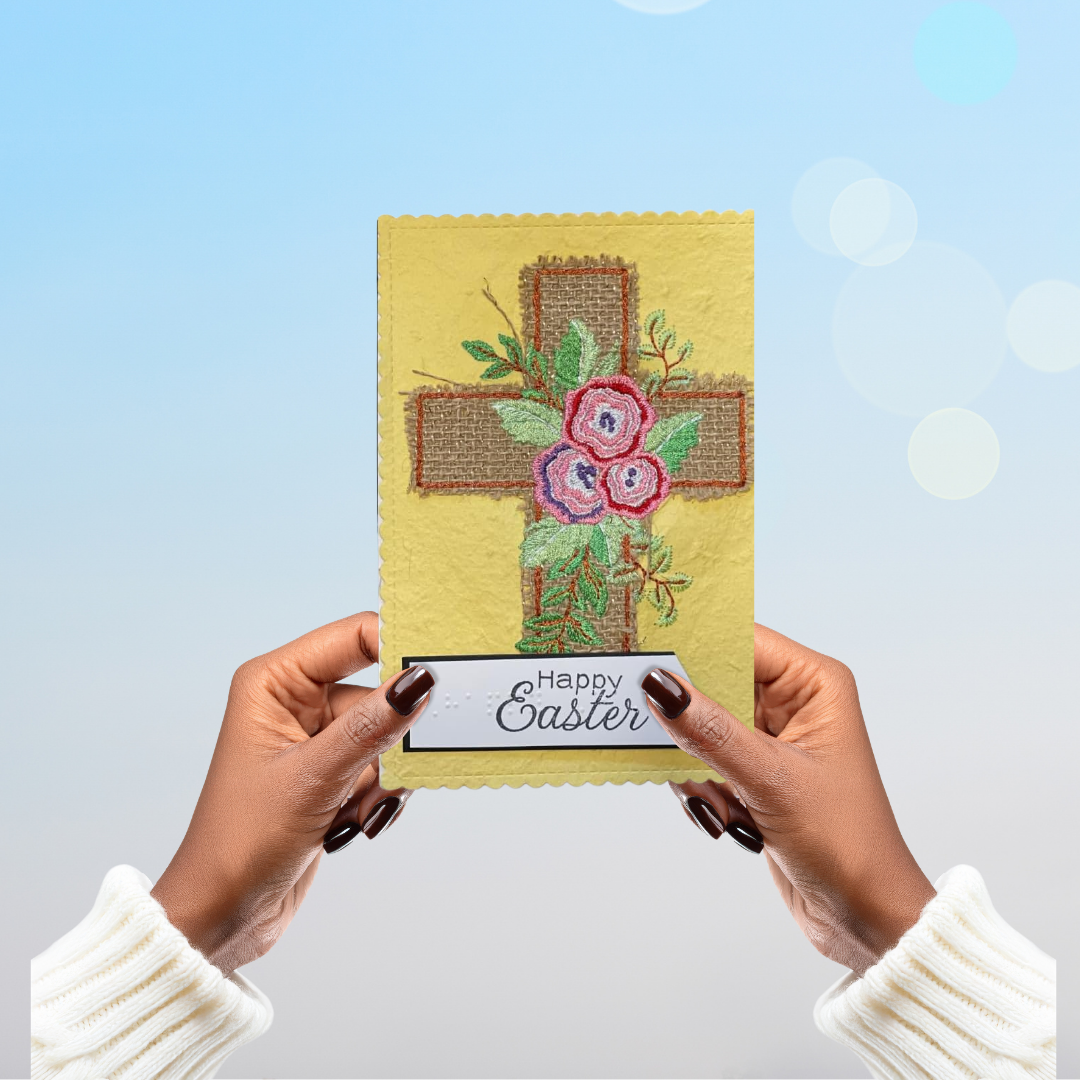 Hands holding a 'Happy Easter' card with floral cross design against a light blue background