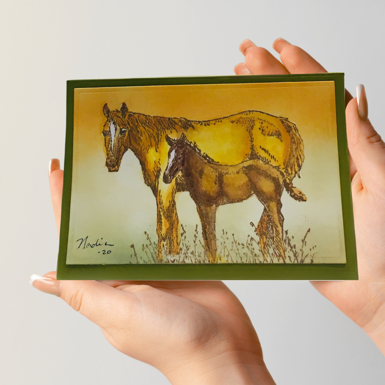 Hand holding a card with a drawing of two horses.