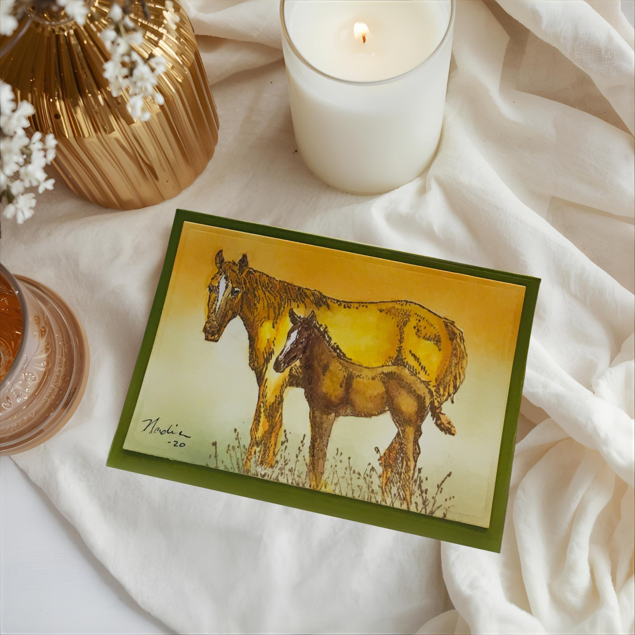 Card with horse illustration on a soft fabric background with a candle and decorative items.