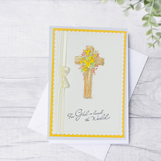 Greeting card with a cross and floral design on a white wooden surface.