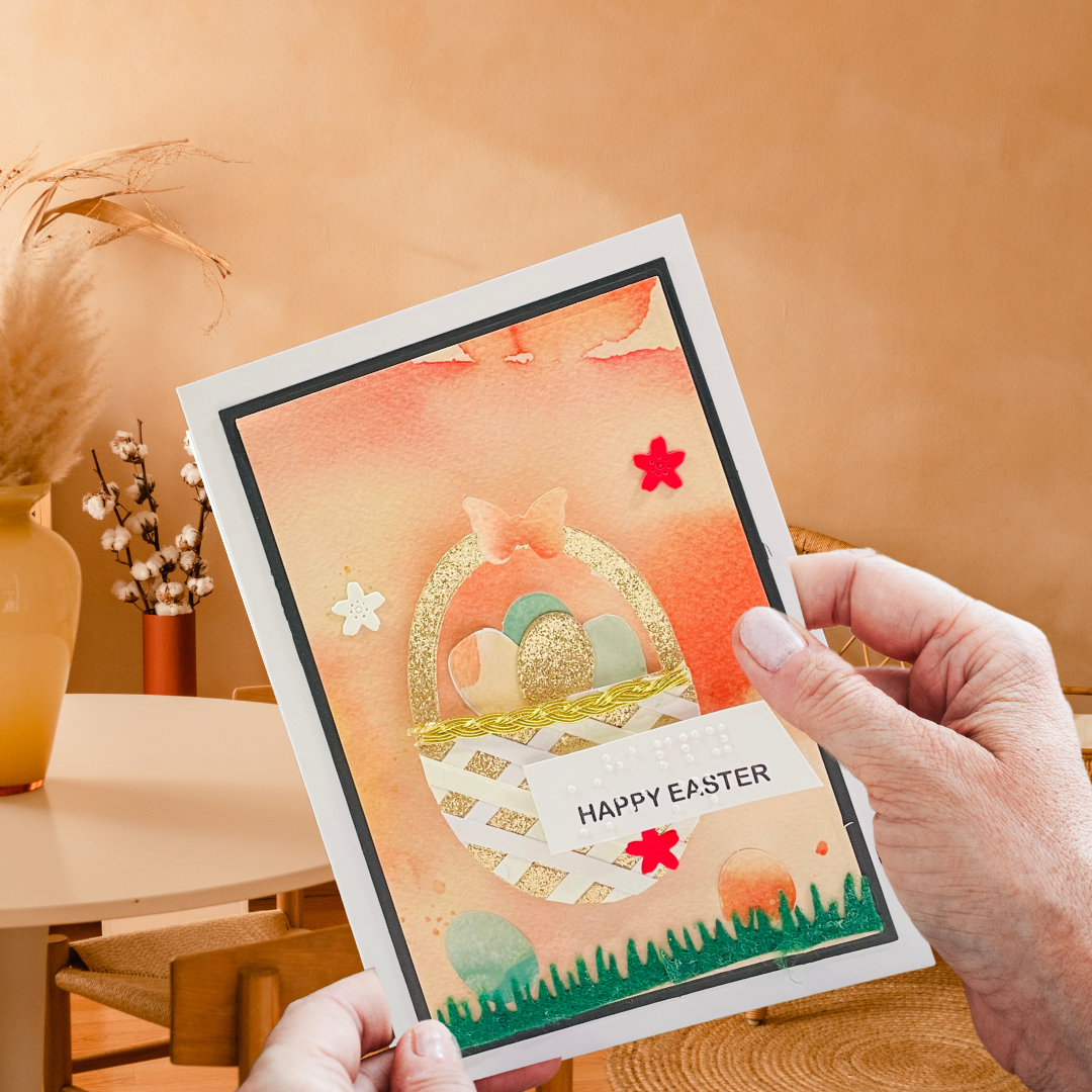 Person holding a 'Happy Easter' card with a decorative design on a wooden surface.