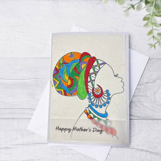 Mother's Day card features a hand-drawn profile silhouette of a woman adorned with a vivid geometric head wrap in orange, red, green, blue, and purple, paired with layered statement jewelry in matching jewel tone on a wooden surface.