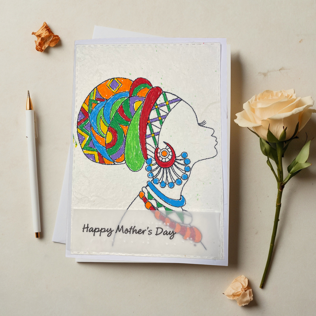 Mother's Day card features a hand-drawn profile silhouette of a woman adorned with a vivid geometric head wrap in orange, red, green, blue, and purple, paired with layered statement jewelry in matching jewel tone 'Happy Mother's Day' text, placed on a light surface with flowers and a pen.