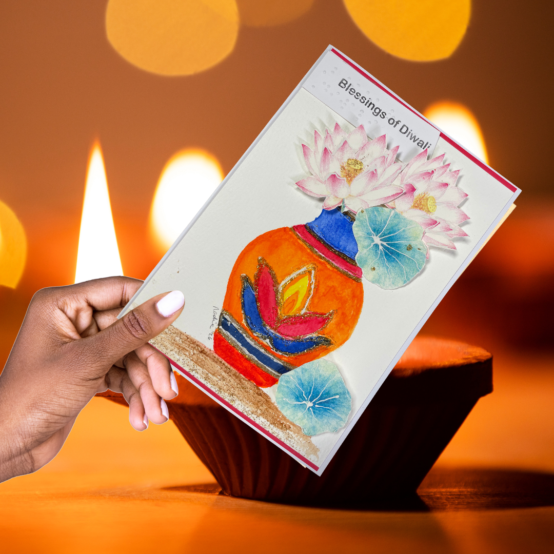 Hand holding a Blessings of Diwali greeting card near a lit diya.
