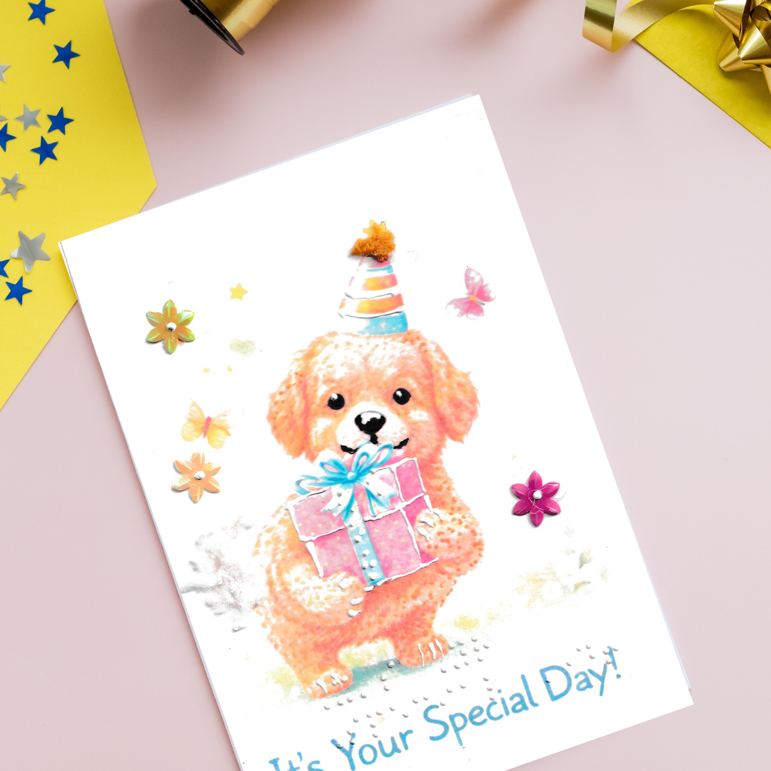 Greeting card with a cartoon dog wearing a party hat and holding a gift, surrounded by flowers on a pink background.