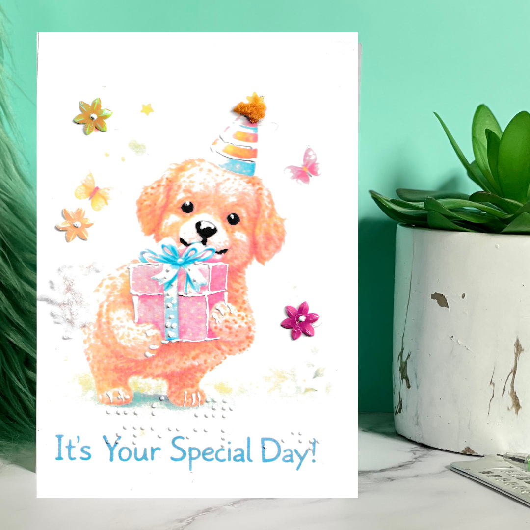 Greeting card with a dog holding a gift and flowers, placed on a marble surface with a plant.