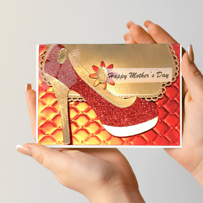 Card with high heel shoe design and 'Happy Mother's Day' text held by hands against a light gray background