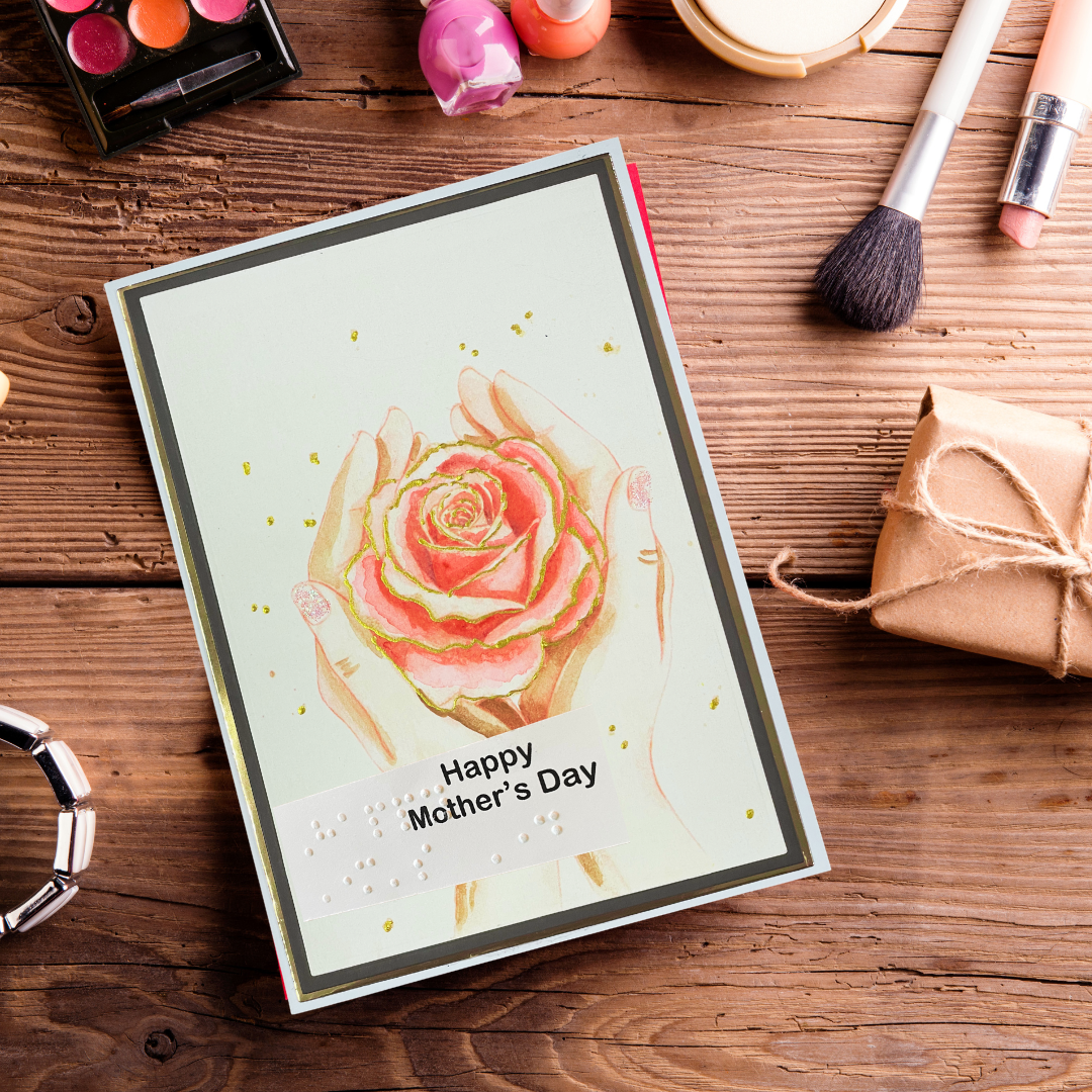 Greeting card with a rose design and 'Happy Mother's Day' text on a wooden surface with makeup items.