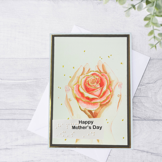 Greeting card with a rose design and 'Happy Mother's Day' text on a light wooden surface.
