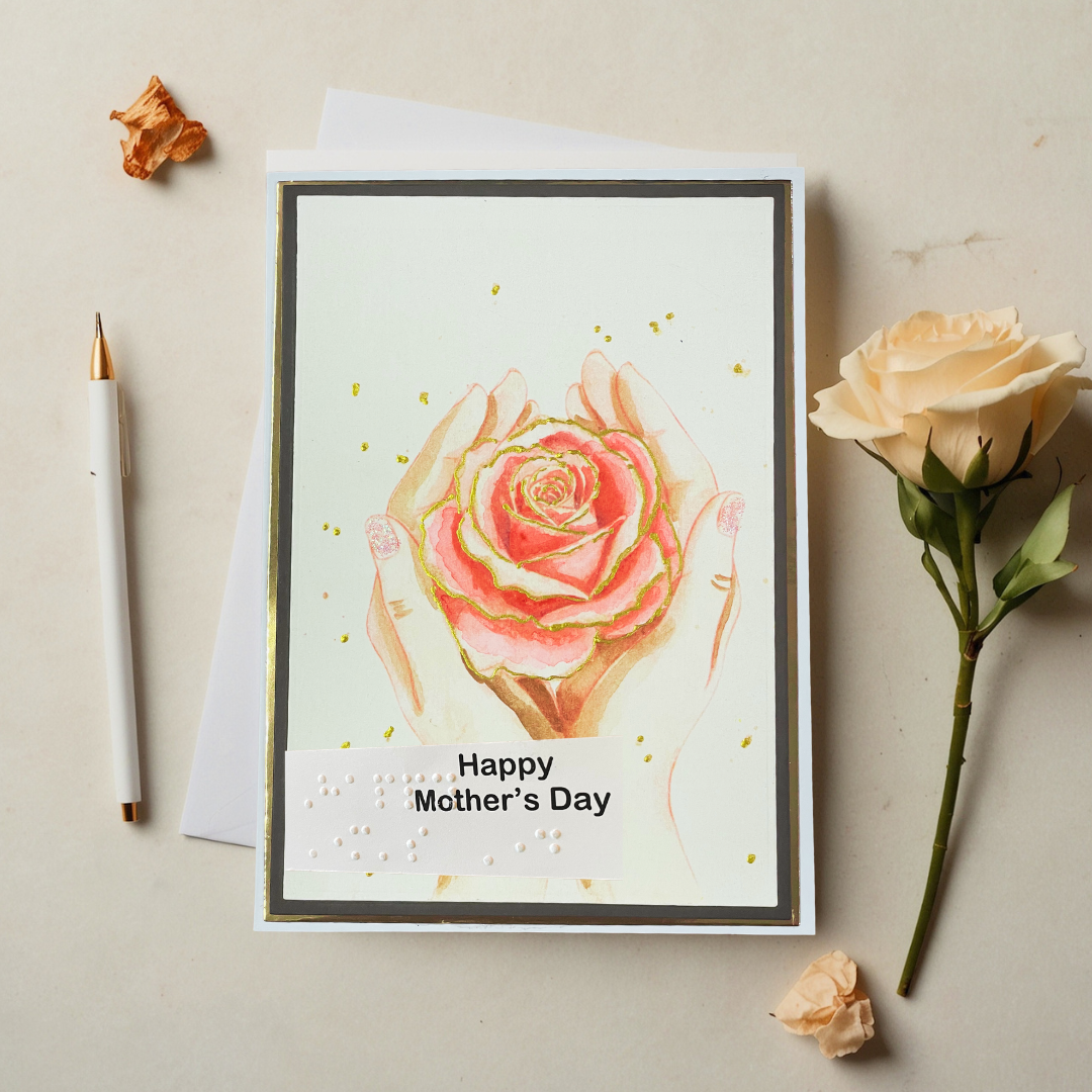 Greeting card with a pink rose and 'Happy Mother's Day' text, surrounded by flowers and a pen on a beige background.