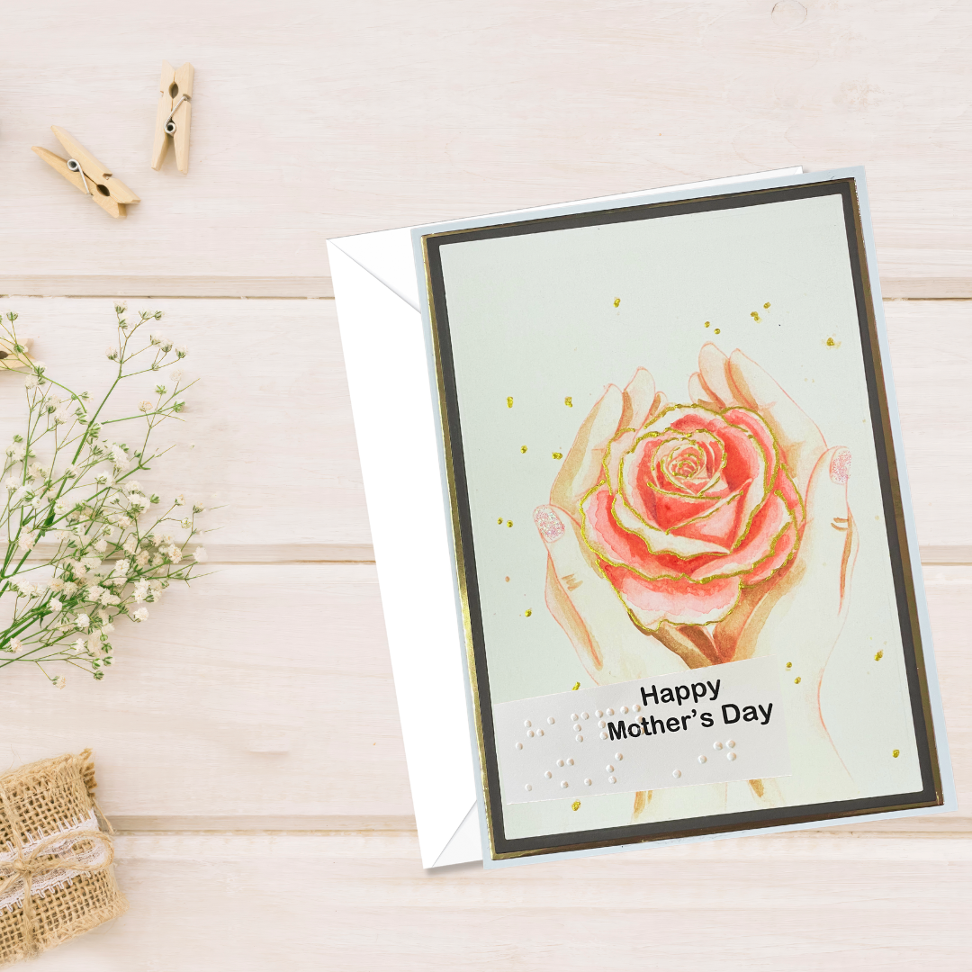 Greeting card with a rose design and 'Happy Mother's Day' text on a wooden surface.