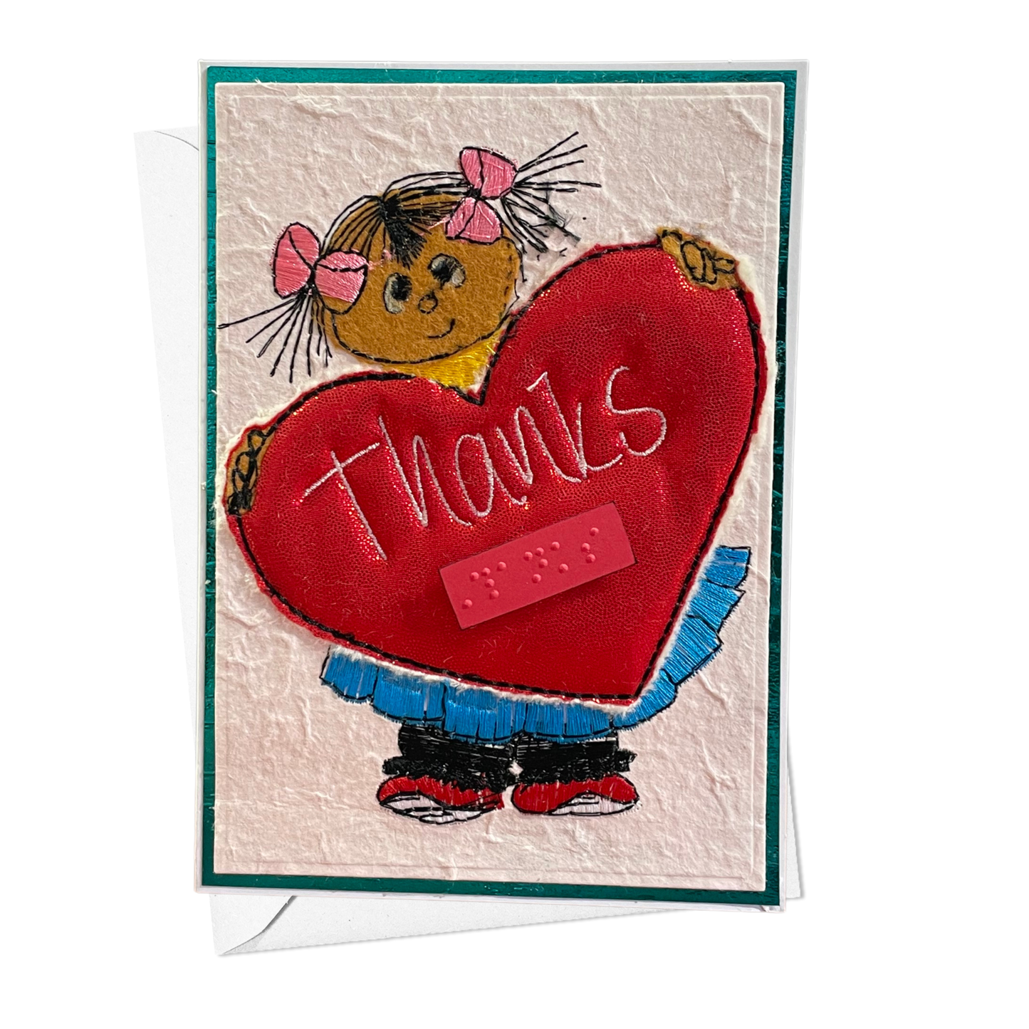 A handmade-style thank you card featuring a cartoon girl with pink bows holding a large red heart that says 'thanks' in white script. The card has a textured cream background, a teal border, and a white envelope partially visible behind it.