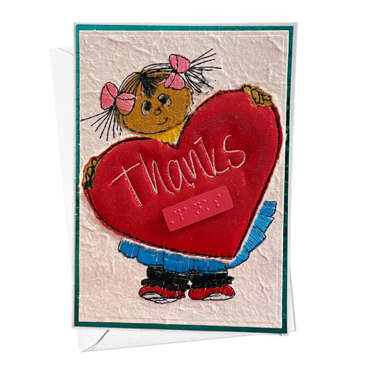 A handmade-style thank you card featuring a cartoon girl with pink bows holding a large red heart that says 'thanks' in white script. The card has a textured cream background, a teal border, and a white envelope partially visible behind it.