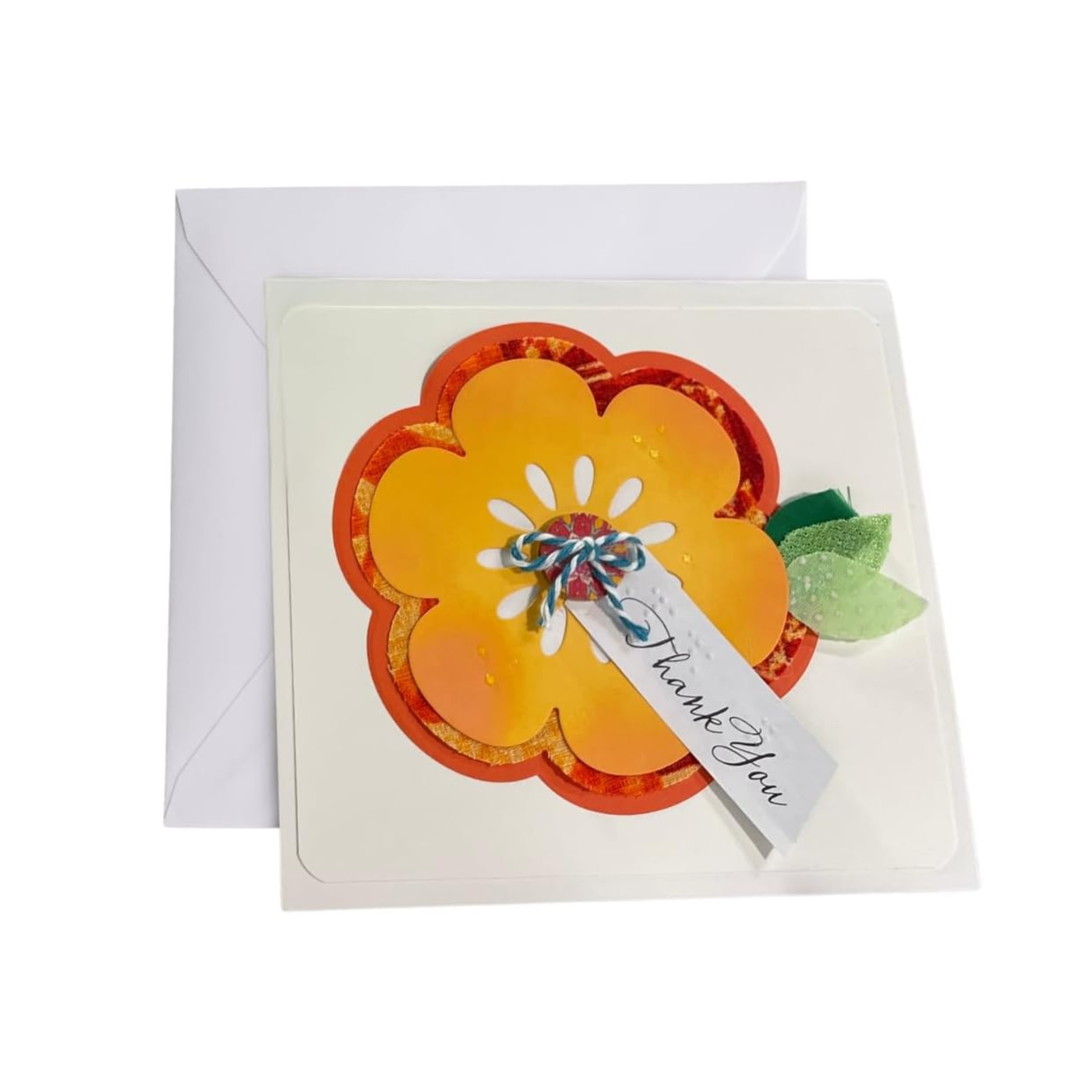 A square white thank-you card with a layered orange and yellow flower design, a small green leaf, and a white tag reading 'Thank You,' shown with a white envelope behind it on a light gray background.